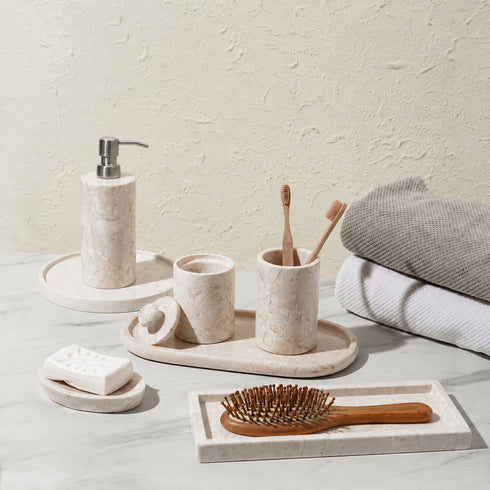 Beige marble soap dispenser with matching toothbrush holder, soap dish and tray in a bathroom