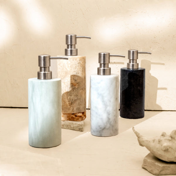 Group of marble soap dispensers in Carrara, Beige, Zeolite and Black stone on a bathroom shelf