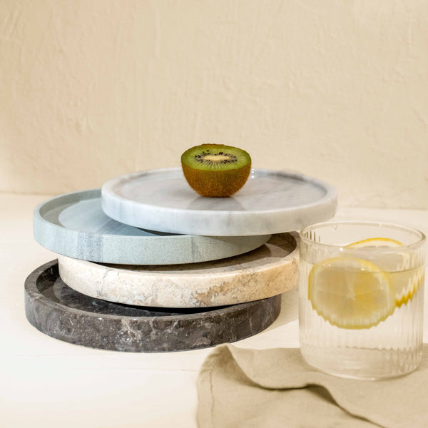 Stack of marble trays with a kiwi and a glass of lemon water on a neutral background