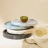 Stack of marble trays with a kiwi and a glass of lemon water on a neutral background