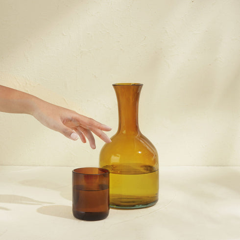 A Hand Reaching for a Glass next to a Brown Carafe Glass