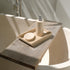 Beige marble soap dispenser on a stone tray beside the bath