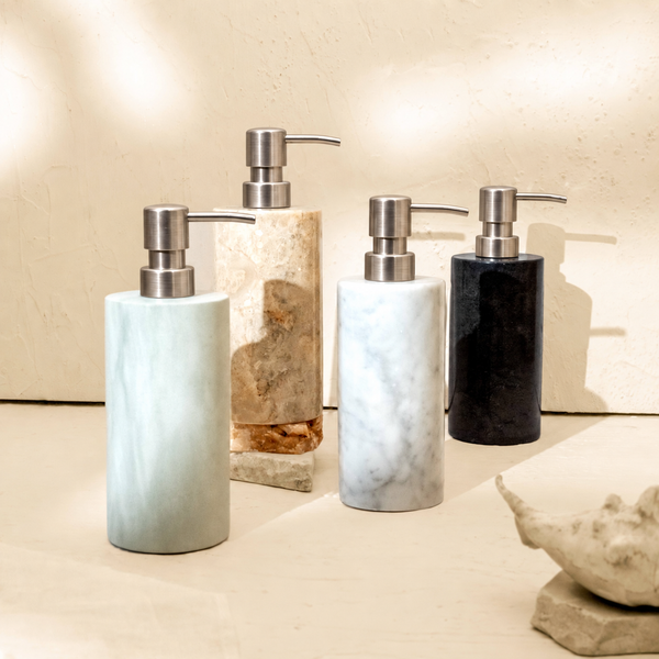 Group of marble soap dispensers in Carrara, Beige, Zeolite and Black stone on a bathroom shelf